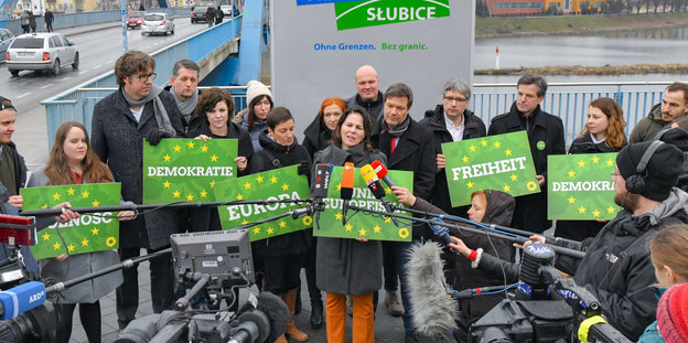 Annelena Baerbock steht vor Mikrofonen, daneben andere Spitzengrüne mit Plakaten wie "Demokratie", "Europa" und "Freiheit"