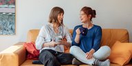 Zwei junge Frauen sitzen auf einem Sofa und trinken Tee