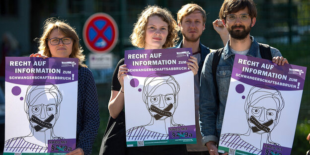 zwei junge Frauen und ein junger Mann demonstrieren mit Schildern gegen den Paragraphen 219a, der Information über abtreibende Ärzte unter Strafe stellt