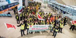Mitglieder der Gewerkschaft Verdi stehen mit Fahnen am Flughafen in einem Terminal