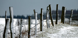 Eine dünne Schneedecke bedeckt bei Temperaturen um null Grad die Landschaft und einen alten Zaun zwischen Sauerland und Siegerland bei Olpe