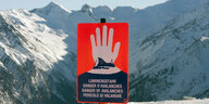 Ein Schild warnt vor einer Bergkulisse vor Lawinen.