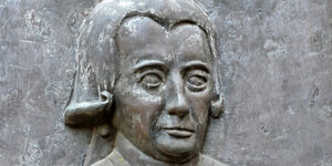 Bronzetafel eines streng blickenden Mannes mit Perücke.