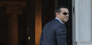 Alexis Tsipras trägt eine Sonnenbrille und blickt über die Schulter nach hinten