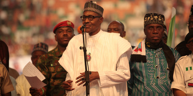 Nigerias Präsident spricht in weißem Gewand und mit Kopfbedeckung zu einer großen Menge