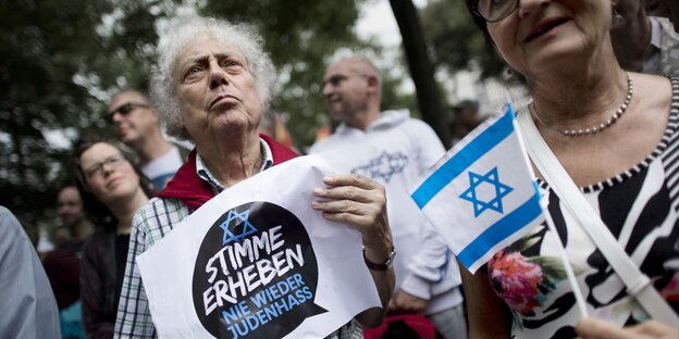 Demonstrantinnen mit einem Plakat mit der Aufschrift „Stimme erheben – Nie wieder Judenhass“ und israelischer Fahne