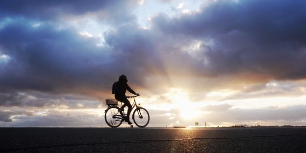 Auf dem Tempelhofer Feld in Berlin fährt ein Mensch im Sonnenuntergang Fahrrad