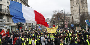Teilnehmer einer «Gelbwesten»-Demonstration marschieren durch Paris, einer hält eine Frankreich-Flagge in die Höhe