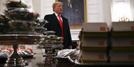 Trump steht hinter einem Tisch, der mit Burgern und Salaten in Plastikschalen vollgestellt ist