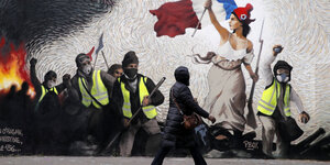 Ein Mann läuft vor einer Wand mit Graffiti entlang, darauf Gelbwesten und eine Frau mit französischer Fahne