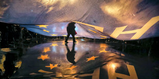 Eine Person läuft unter einem großen Banner durch. Auf dem nassen Boden spiegeln sich die Lichter