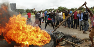 Mehrere Demonstranten stehen in Harare vor einer brennenden Straßensperre