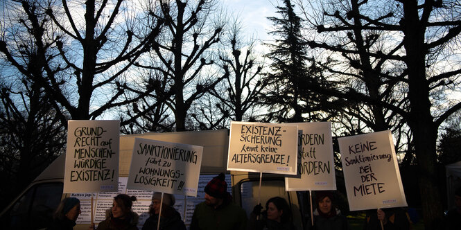 DemonstrantInnen mit Schildern stehen vor kahlen Bäumen