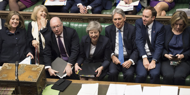 Theresa May sitzt zwischen mehreren Menschen auf einer Bank im House of Commons