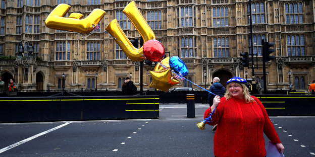 Frau im roten Pulli hält goldene Luftballons in Form der Buchstaben E und U in die Höhe