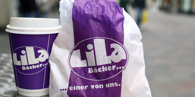 Eine Tüte und Kaffee-Becher mit dem Logo der Lila Bäckerei.