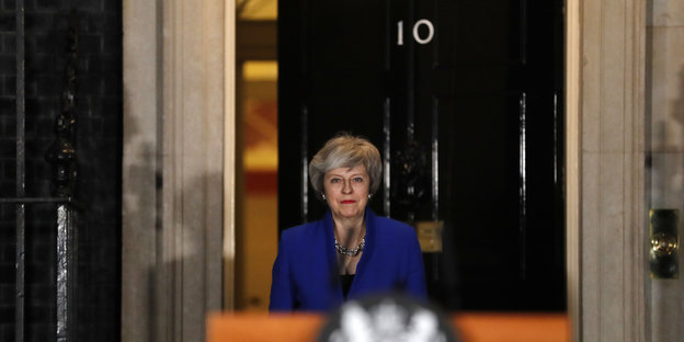 Theresa May in blauem Jackett guckt durch eine Tür