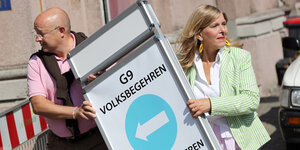 Ein Mann und eine Frau stellen ein Schild der Initiative "G9-Jetzt-HH" auf.