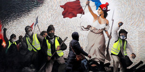 Eine Frau geht vor einem Wandgemälde auf einer Mauer vorbei, auf dem Gelbwesten-Demonstranten zu sehen sind