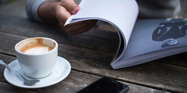 Eine Person liest, daneben steht eine Tasse Kaffee