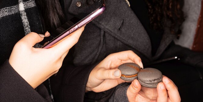 Mit einem rosa Smartphone werden zwei dunkelgrauen Macaron fotografiert