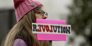 Eine Frau mit pinker Mütze und einem Schild, auf dem "Revolution" steht.