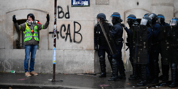 Ein Mann nimmt ein Selfie vor einem Grafitto auf, daneben stehen mehrere Polizisten