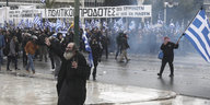 Auf den Straßen Athens protestieren Menschen mit Griechenland-Flaggen. Sie tragen Gasmasken
