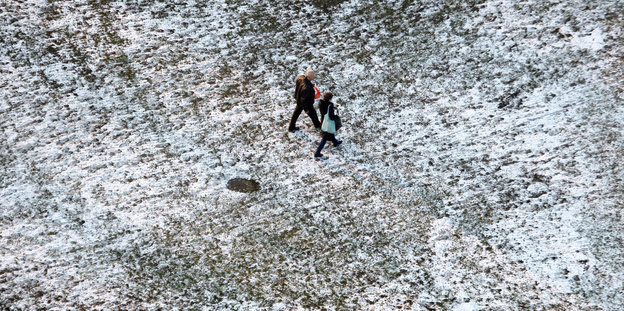 Passanten gehen auf dem Messegelände in berlin über eine verschneite Wiese