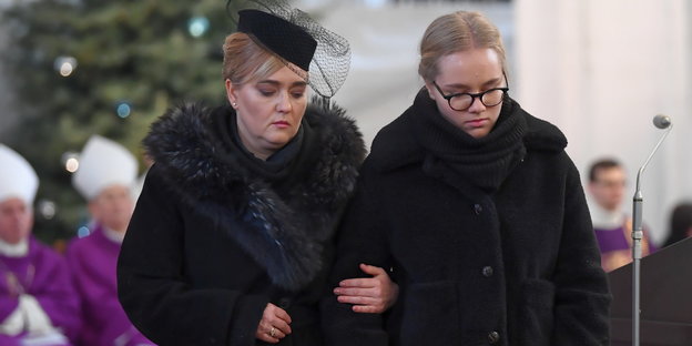 Zwei Frauen in Trauerkleidung haben sich beieinander untergehakt