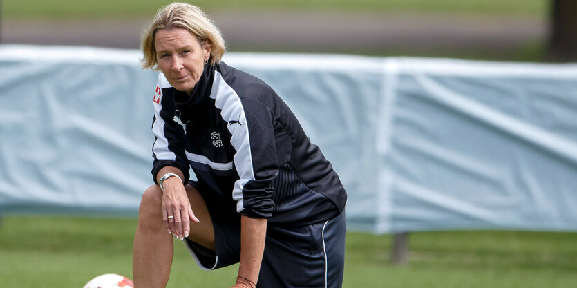 Martina Voss-Tecklenburg kniet auf einem Fußballplatz