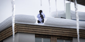 Aus einem mit Schnee bedeckten Dach steht ein Mann in weißer Jacke mit Maschinengewehr