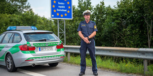 Ein Polizist steht auf der Straße vor seinem Polizeiwagen