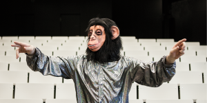 Ein Mensch mit Affenmaske steht in einem Hörsaal.