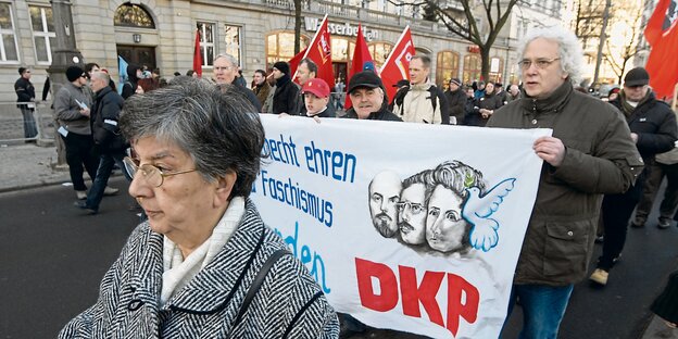 Demonstranten mit grauen Haaren tragen ein Plakat der DKP.