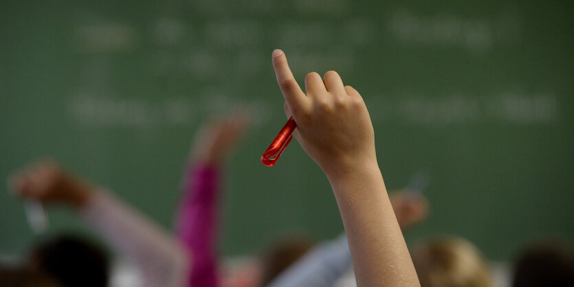 Vor einer Schultafel wird eine Hand gehoben