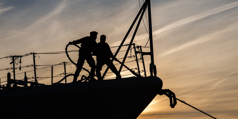 Zwei Marinesoldaten stehen am frühen Morgen vor der aufgehenden Sonne auf dem Bug der „Augsburg“