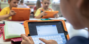 Eine Schülerin tippt auf einem Tablet, gegenüber sitzen zwei weitere Schüler mit Tablets