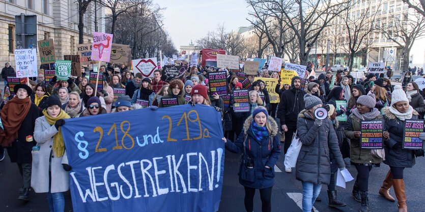 Auf einer Straße stehen zahlreiche Demonstrantinnen vor einem Transparent "Paragraf 218 und 219a wegstreiken!"