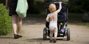Ein Kleinkind, das nur eine Windel trägt, schiebt einen Kinderwagen in einem Park