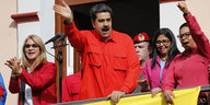 Nicolas Maduro in roter Arbeiter-Uniform steht auf einem Balkon und winkt heroisch