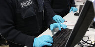 Polizisten mit Handschuhen tippen auf einer Tastatur