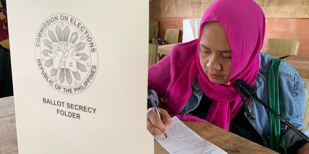 Eine Frau mit einem pinken Kopftuch füllt einen Wahlzettel aus
