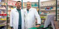 Zwei Apotheker stehen in Kitteln vor Regalen mit Medikamenten