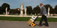 Ein Mann schiebt eine Karre mit Dingen an einem Park entlang