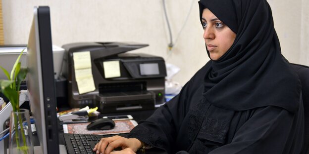 Eine Frau in einer saudischen Abaja sitzt an einem Computer.