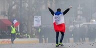 Eine Person hat sich eine französische Flagge umgehängt und reckt die Arme in die Höhe