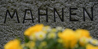 Gedenktafel mit Blumen und dem Wort "Mahnen"