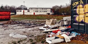 Müll liegt auf einer Brache, dahinter sind die Wohncontainer in der Luruper Hauptstraße.