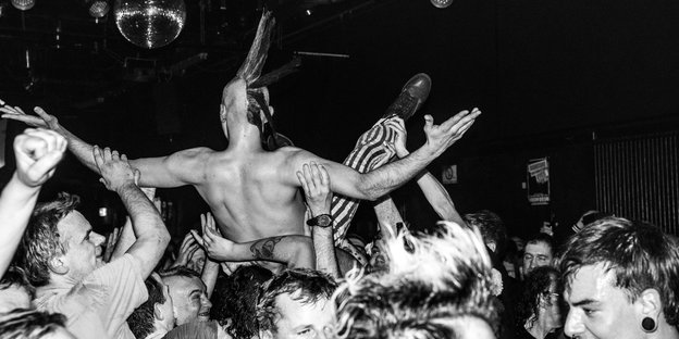 Die Schwarzweißaufnahme zeigt einen Mann mit Iro, der sich von der Menge durch den Berliner Punkclub SO36 tragen lässt. Nicht im Bild die Band: Die UK Subs gibt es schon seit über vierzig Jahren.